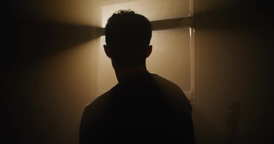 Man stands silhouetted by sunlight entering dark room through window