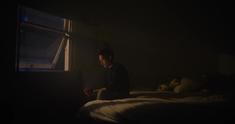 A man sitting on the edge of a bed looking out a window