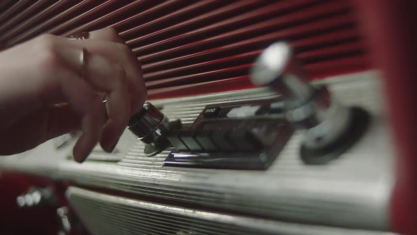 Woman pushing buttons and turning knobs on a vintage stereo on a car dashboard