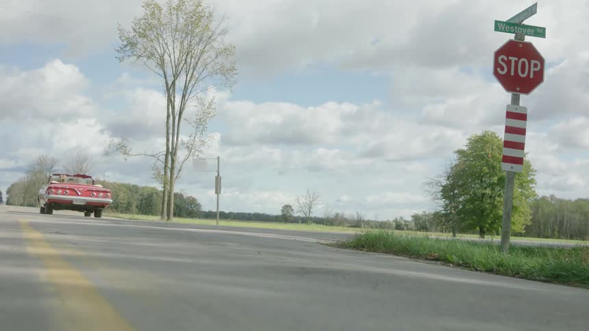 A woman runs a stop sign while driving a vintage red convertible