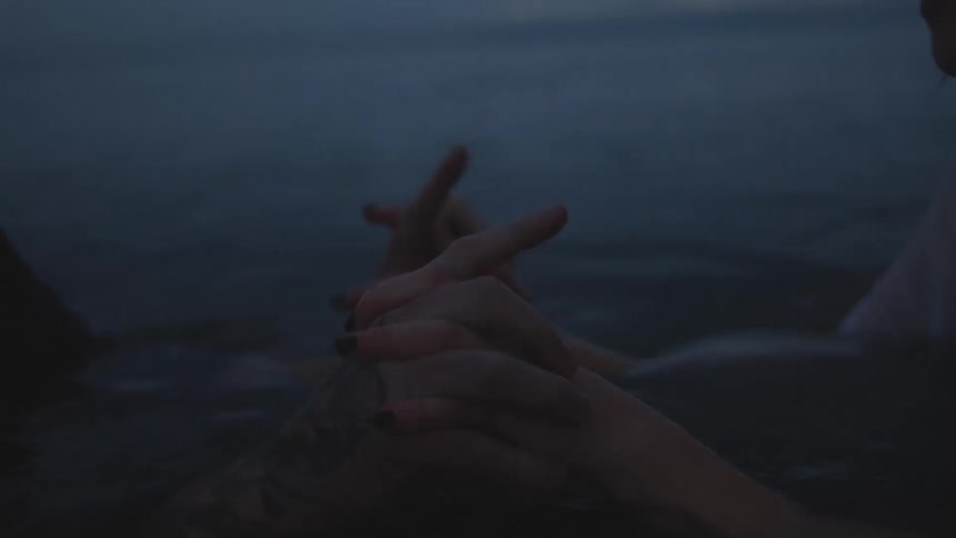 Two people are holding hands and interlacing fingers as they sit in the water