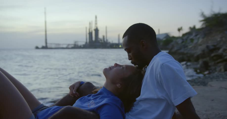 A man kisses a womans forehead as they sit relaxing on an ocean beach after sunset