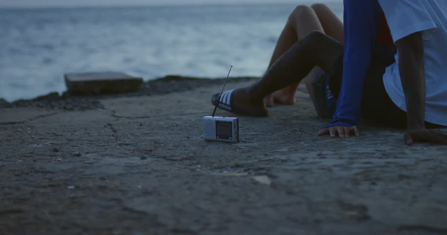 A couple is sitting close together on a beach on the waterfront