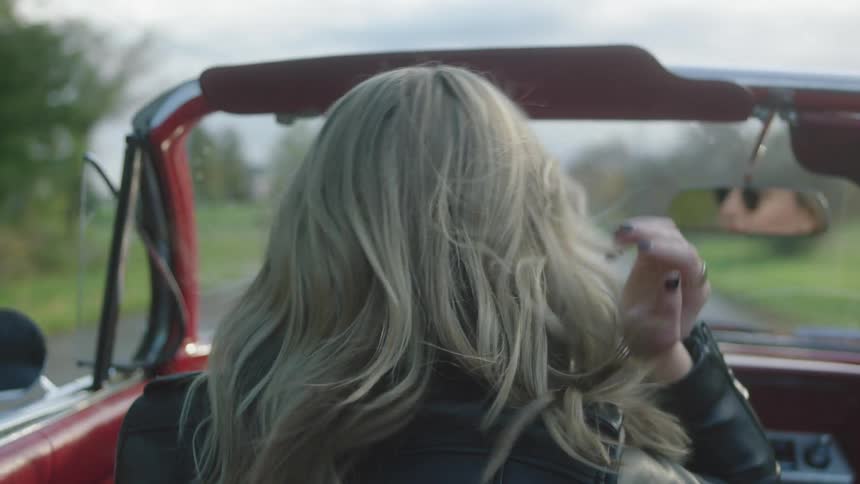 A woman drives down the empty road in her convertible