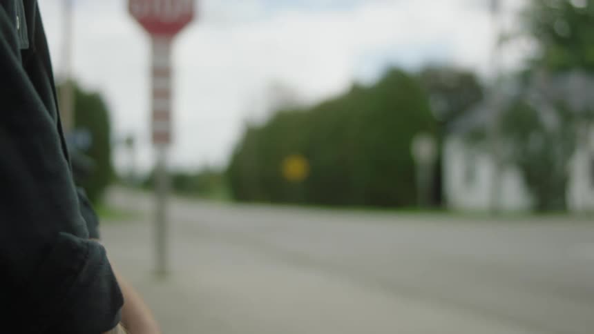 Partial view of a man standing on the side of a street sticking his thumb out trying to hitch a ride from a passing white car