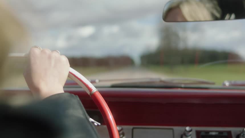 Blonde woman steers vintage car along highway