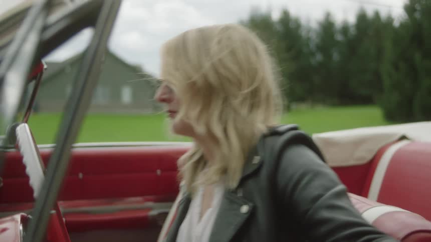 A woman flicks a cigarette on the ground then climbs in a car to drive away