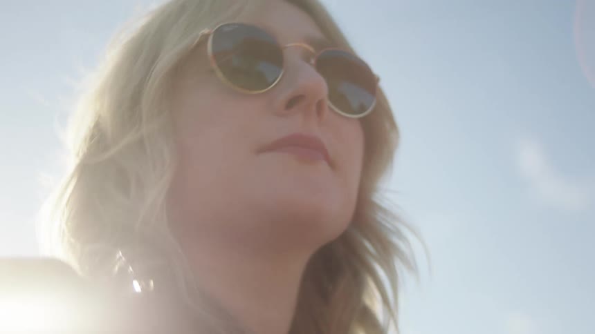 Young woman wearing sunglasses and black leather jacket driving a car in the countryside