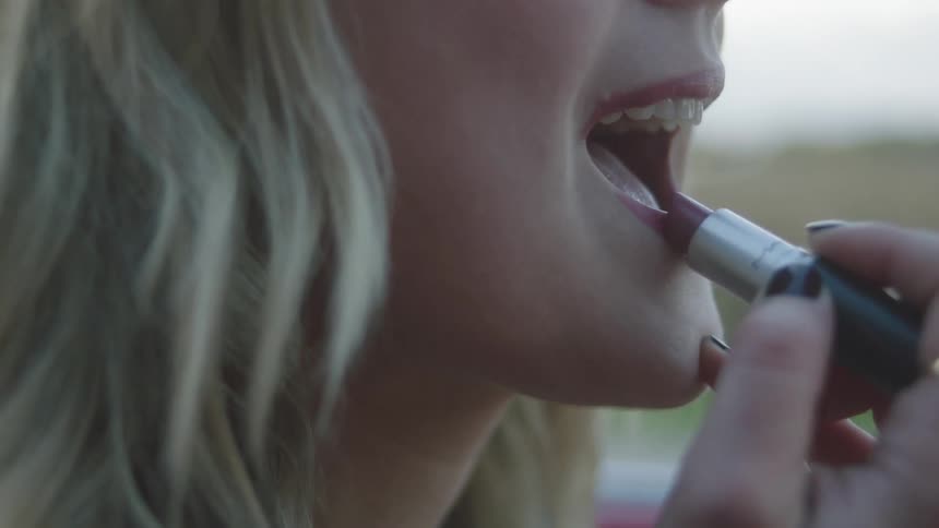 A woman applies lipstick while sitting in her car