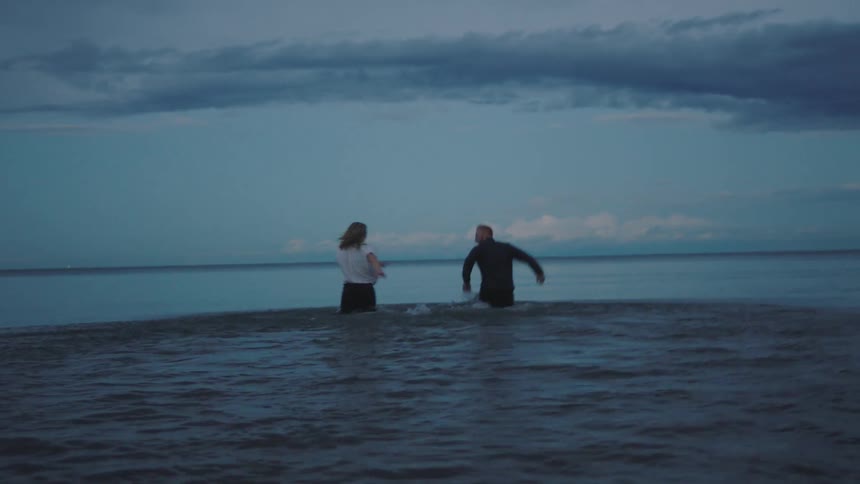 A man and woman run into the water and splash around