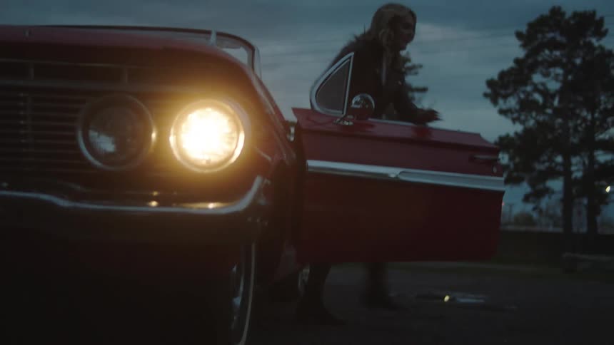 Woman parks vintage convertible with its headlights on and runs as male passenger playfully chases her