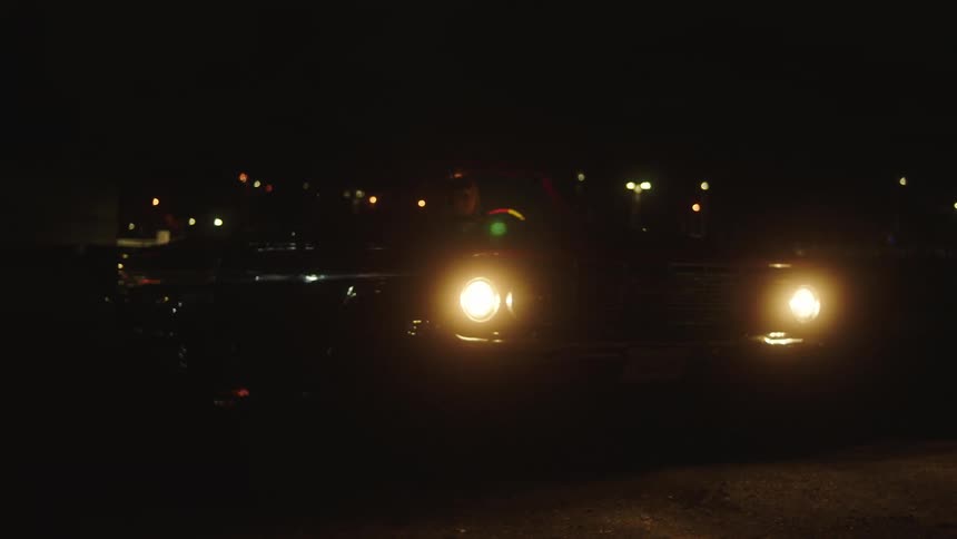 Woman pulls out in convertible as traffic passes behind her on highway at night
