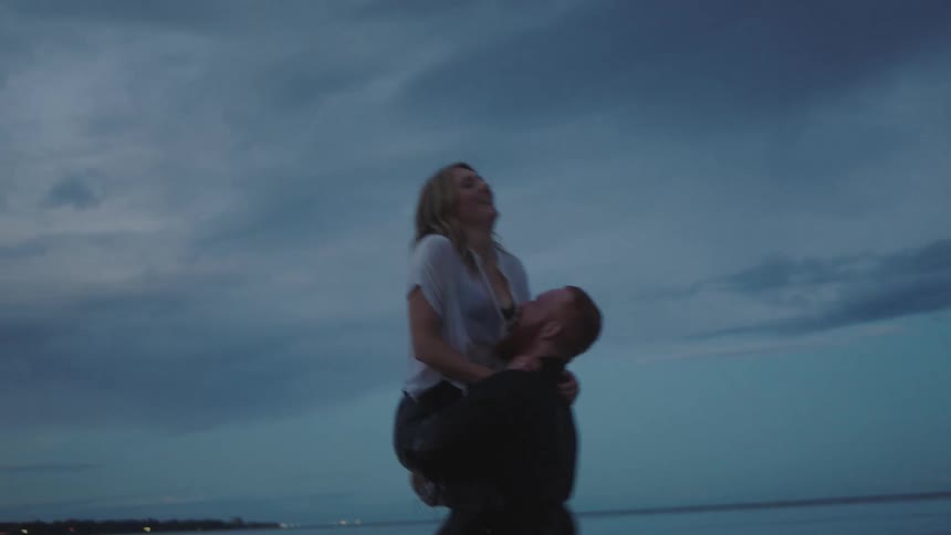 A fully clothed man and woman splash and play in the ocean