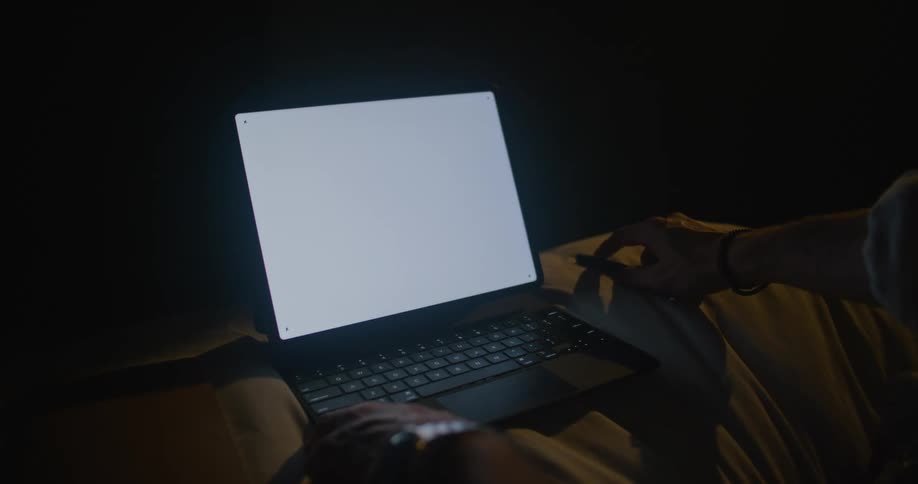 Man sits in front of laptop place on soft surface in dark room