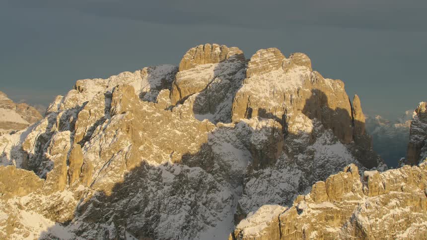 Snow clings to the sides of steep mountain peaks under a dark sky