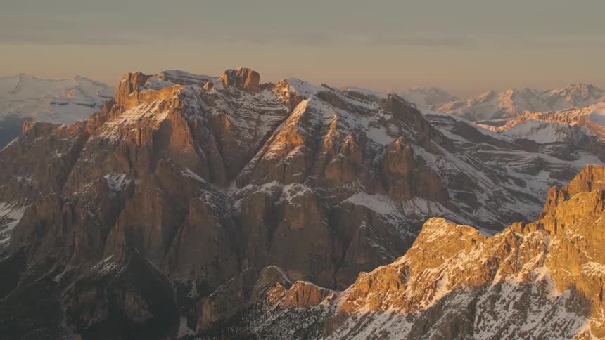 A mountain range covered in patches of snow in the evening