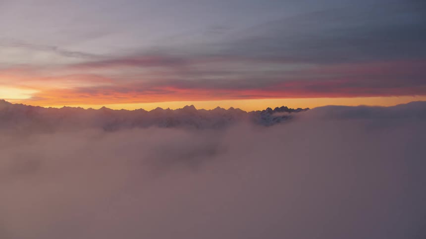 Clouds moving in front of a snow covered mountain range high in a colorful cloudy red sky