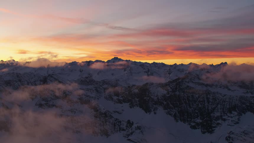 Snow covered mountain range high in the clouds and a colorful red sky