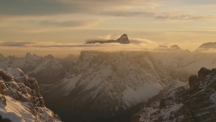 The peak of a snow covered mountain peaks through clouds in the evening