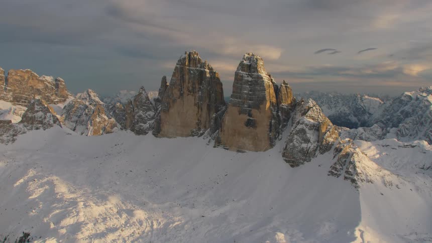 Rock crags are sticking out of a snow covered mountain range at sunrise