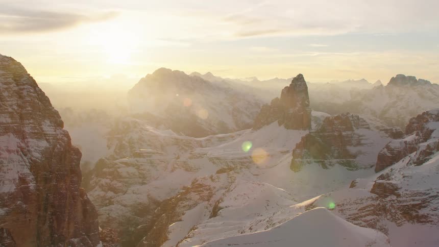 The sun is shining brightly on snow covered mountains with peaks high in a cloudy sky