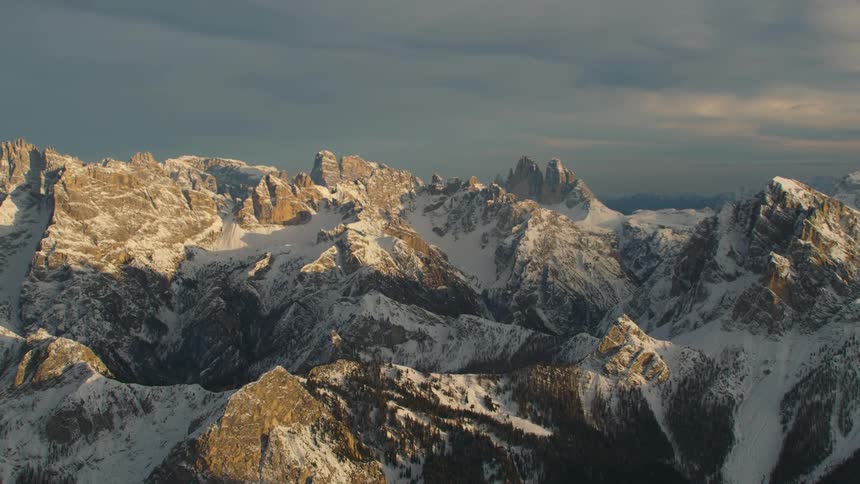An aerial view of snowy mountains in the evening with an overcast sky