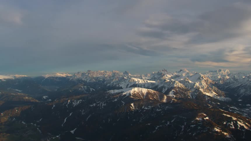 A vast mountain range partially covered in snow at sunrise
