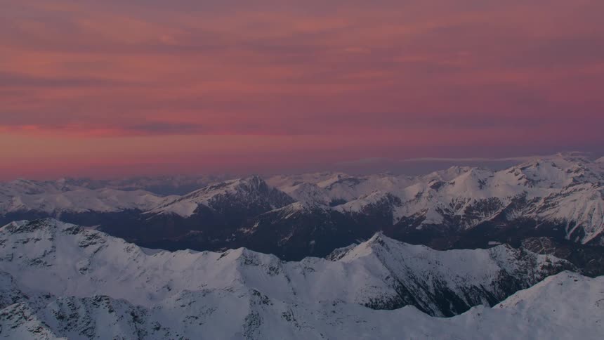 Mist covers snowy mountains under red cloudy sky