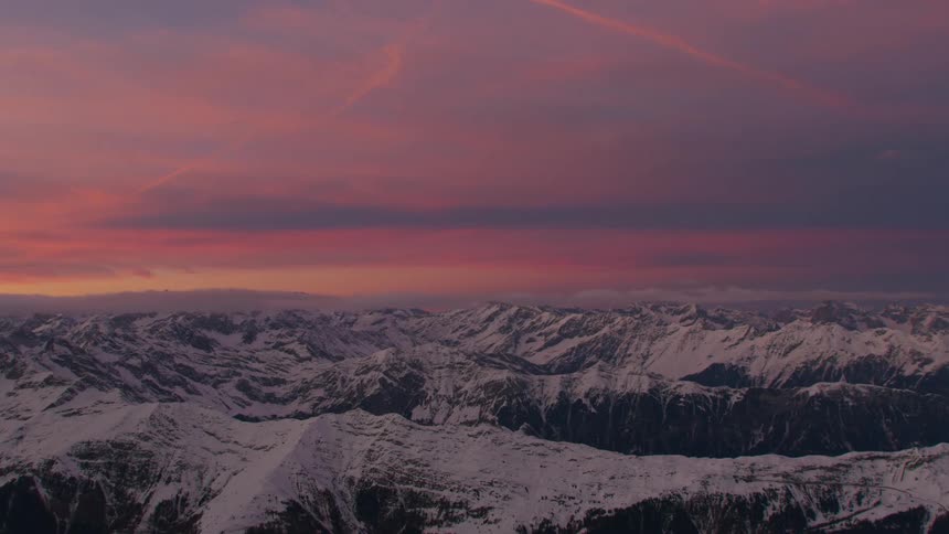 A snow capped range of mountains under a purple sky at sunset