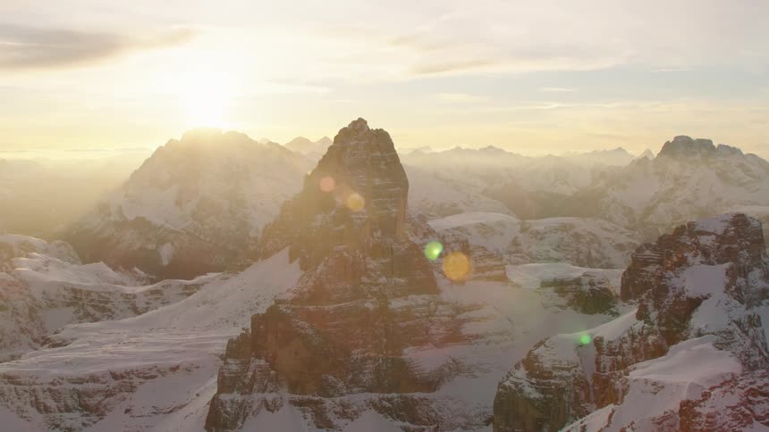 Sun glares from sky onto snow covered mountain range on misty day