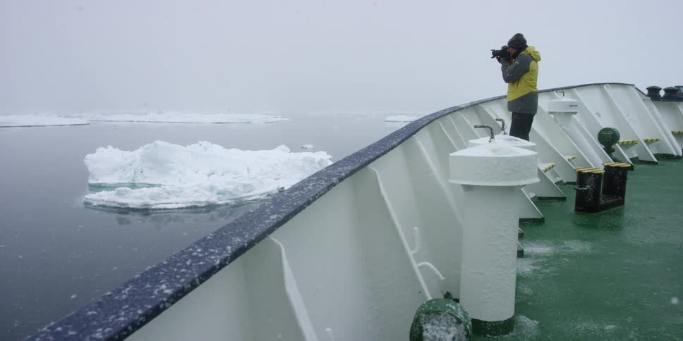 Man taking pictures from a large boat in a frozen wilderness