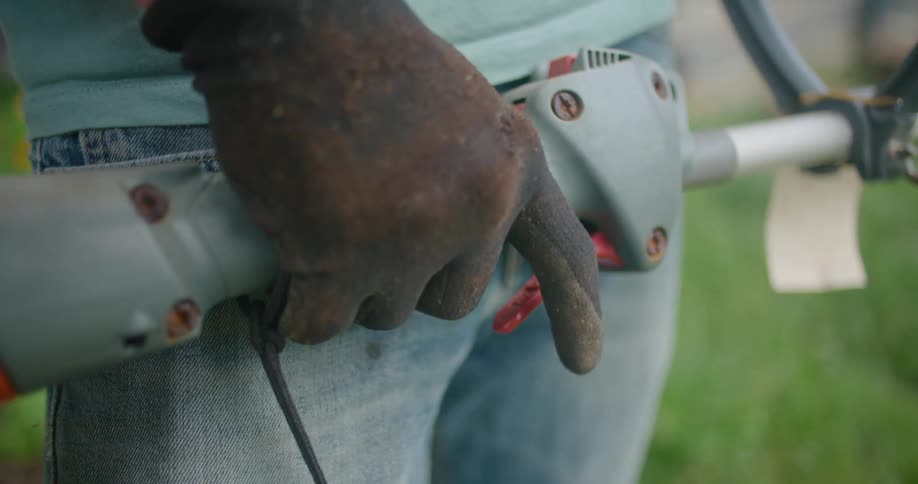A man keeps pressing the trigger on a trimmer as he stands on a lawn