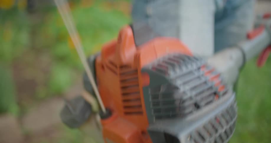 A person starts a weed whacker to trim weeds in a yard