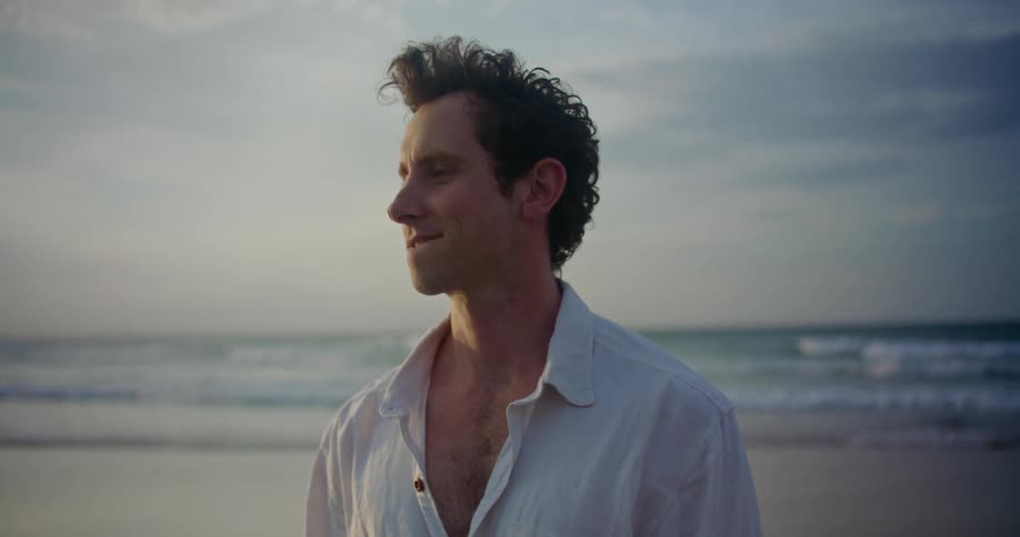 A man is standing on a beach while thinking and smiling in the daytime