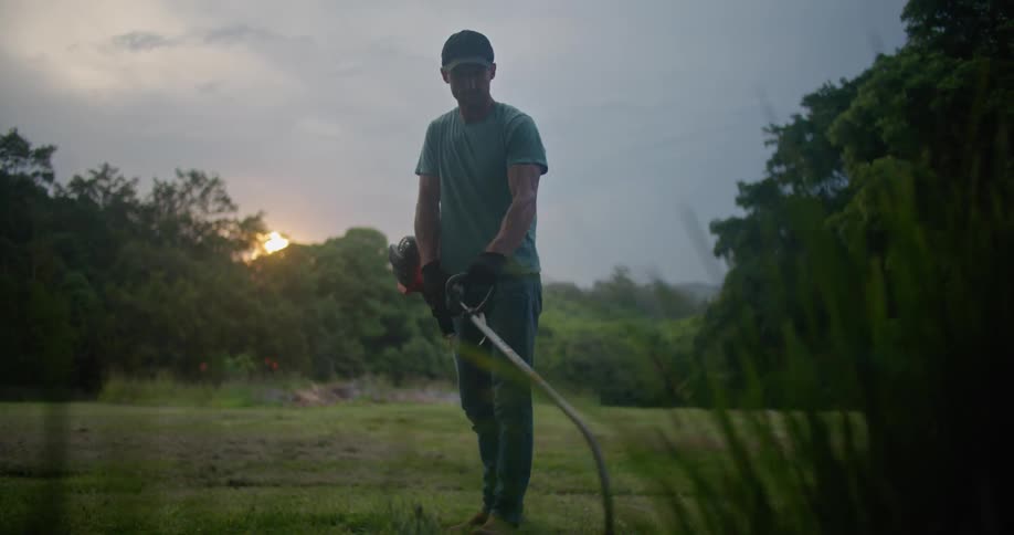 A man stands in a grassy field and edges the lawn