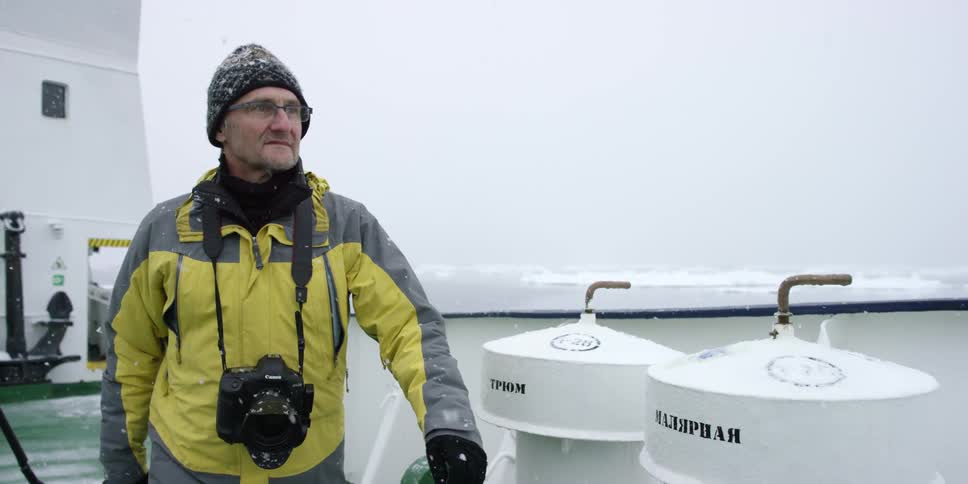 A man in a yellow jacket walks on a snowy boat