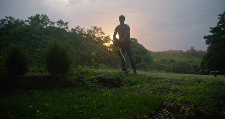 A man uses a gas powered weed whacker to trim the edges of a grassy area