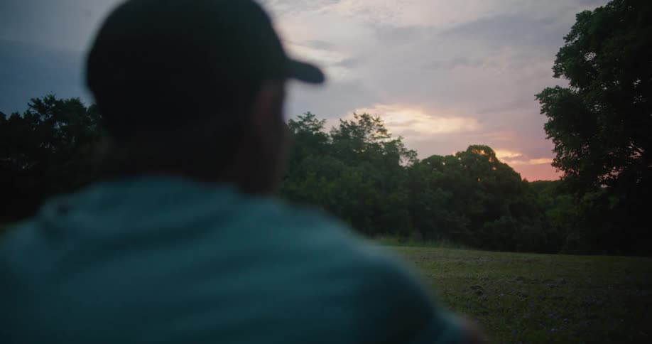 A man wearing a baseball cap is looking around at trees