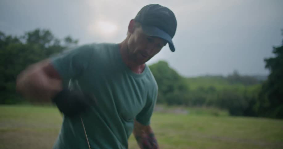 A man is standing in a field and trying to start a gas powered string trimmer