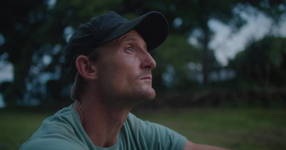 Man wearing baseball cap sits on ground in field