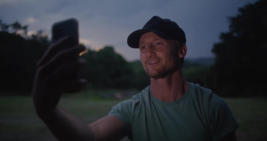 Young man standing on a field at evening neds a call on his smartphone
