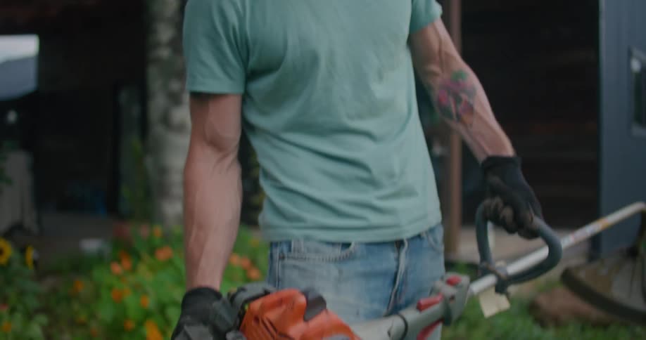 A man is holding a gas powered string trimmer in a front yard