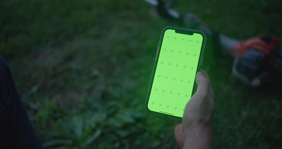A person is outside holding their phone over some grass