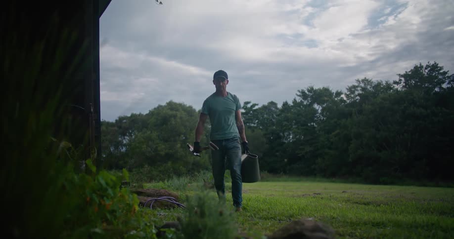 A man picks up a shovel and bag and walks away with them