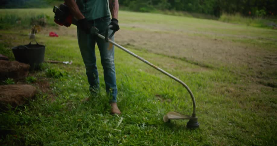 A man in a grassy field trims the grass with a power tool