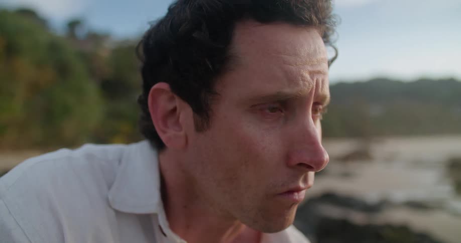 The face of a tearful man sitting and thinking on an isolated beach in the daytime