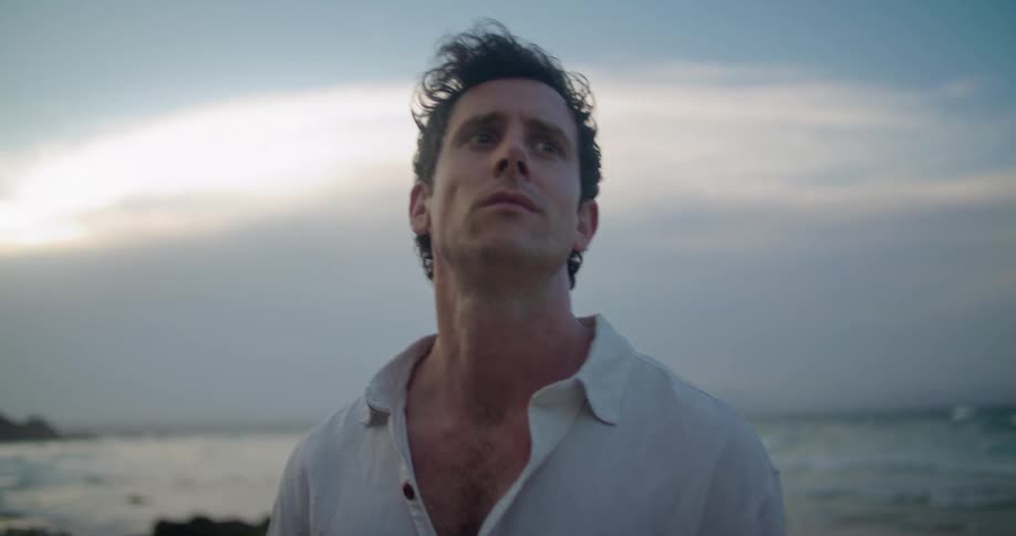 Man stands on windy beach sighing as he looks around
