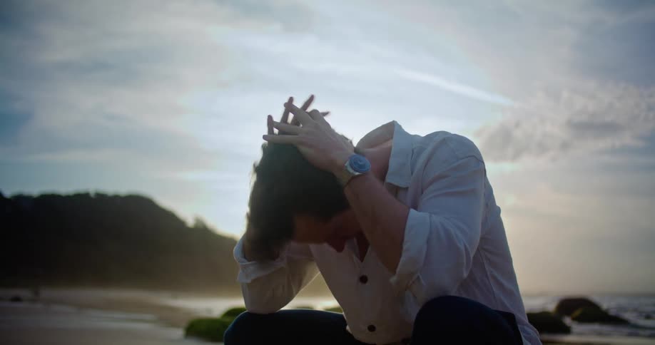 A man is sitting on a beach and thinking about something thats worrying him in the evening