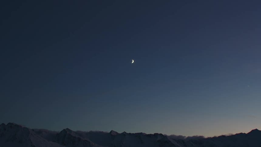A crescent moon is surrounded by twinkling stars over a mountain range