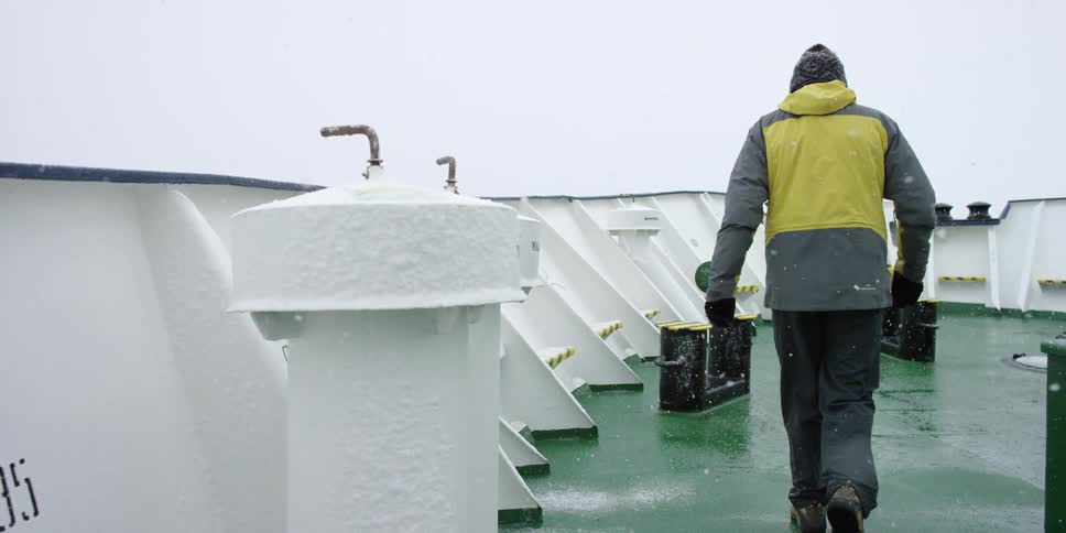 Person wearing warm clothes walks across the ship's deck in the snow
